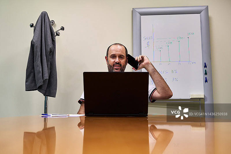 在办公室工作时使用手机的微笑商人。工作概念。图片素材