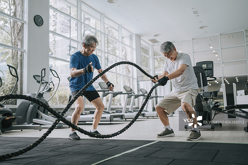 年长的私人教练鼓励年长的男人在健身房练习战绳图片素材
