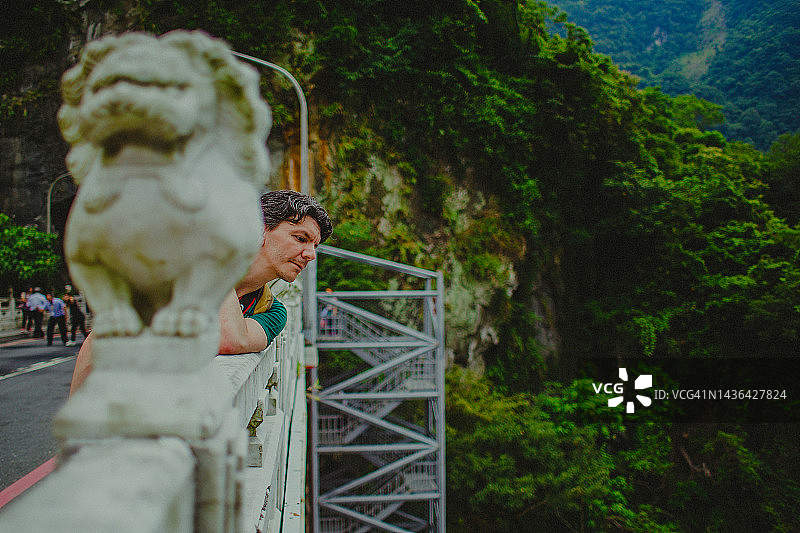 一位中年男子在太鲁阁峡谷的桥上眺望，那里有一座中国台湾大理石狮子雕像图片素材
