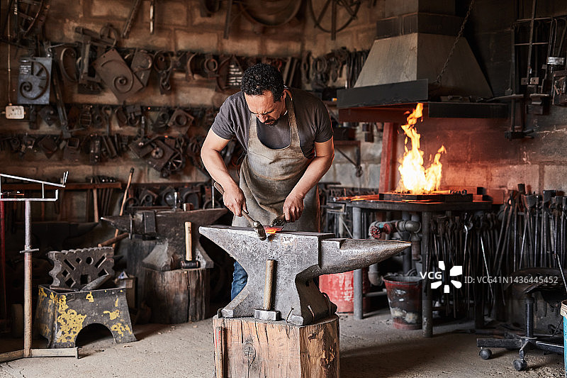 铁匠车间：金属和钢铁生产行业的专业人员。铁砧、手柄锤和工人在工业制造或仓储工作室中使用老式锻造工艺工具图片素材