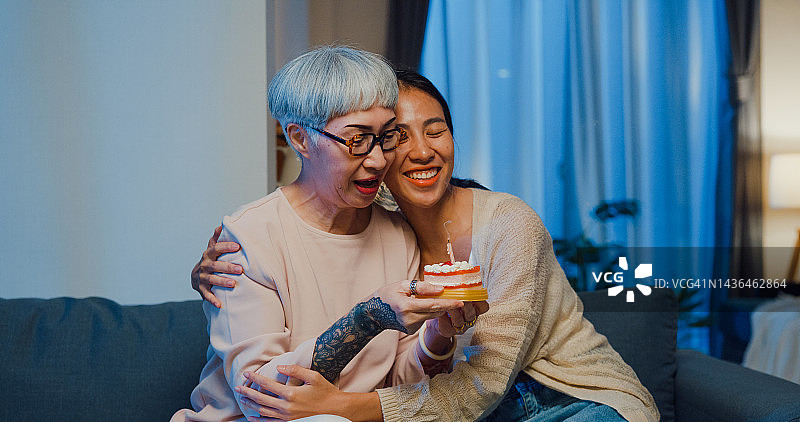 快乐的亚洲女儿惊喜地给坐在沙发上的退休母亲送生日蛋糕图片素材