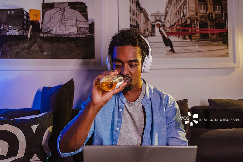 在家使用笔记本电脑并喝啤酒的年轻男人图片素材