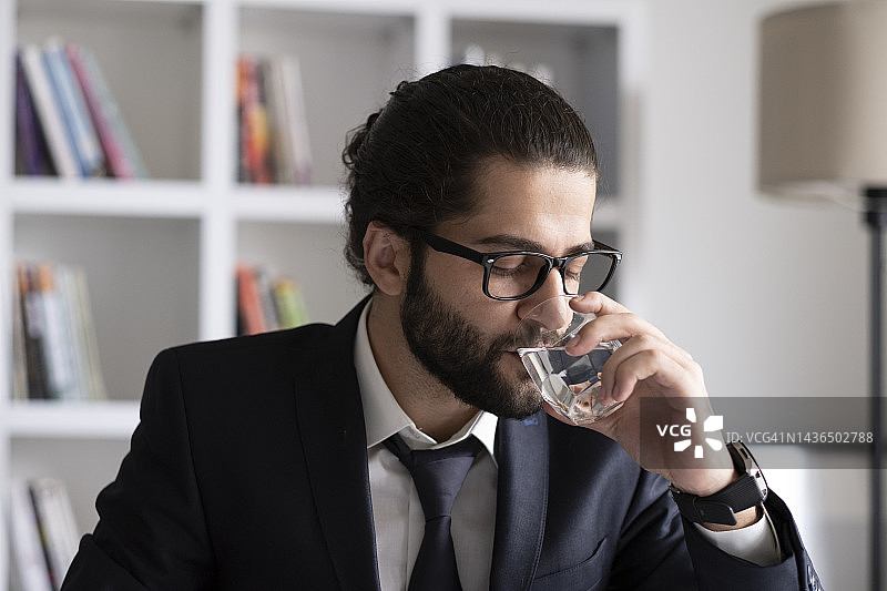 年轻商人在办公室一边喝水一边用笔记本电脑工作图片素材