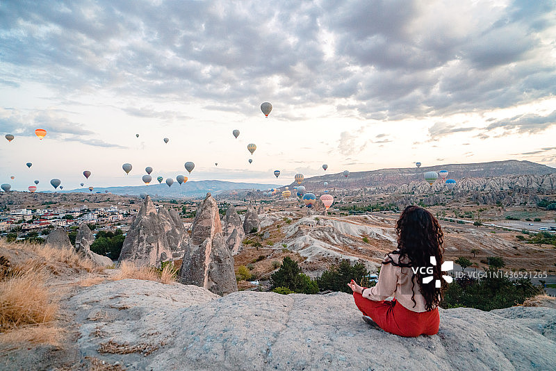 女背包客在土耳其卡帕多奇亚格雷梅冥想和做瑜伽，同时观赏热气球图片素材