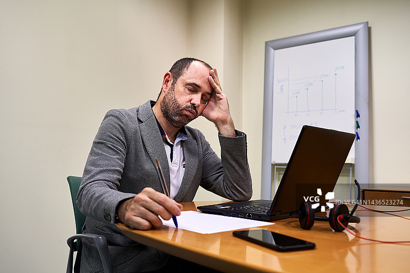 疲惫的商人在创意金融办公室坐在办公桌旁看着笔记本电脑。工作概念。图片素材