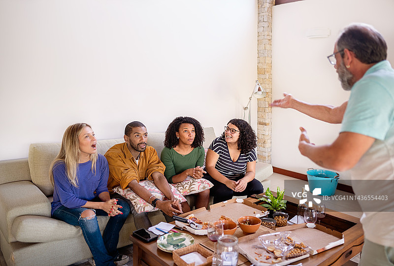 在聚会期间与朋友玩猜谜游戏的中年男人图片素材