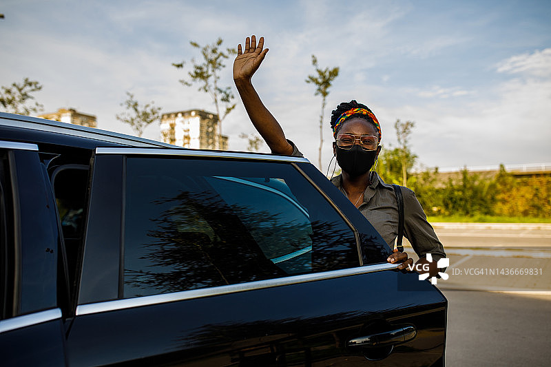 年轻女人站在汽车后门旁，向朋友挥手图片素材