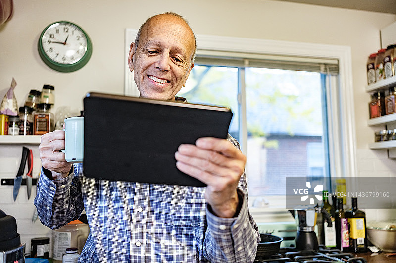 年长的男人在厨房里用平板电脑观看和收听广播图片素材