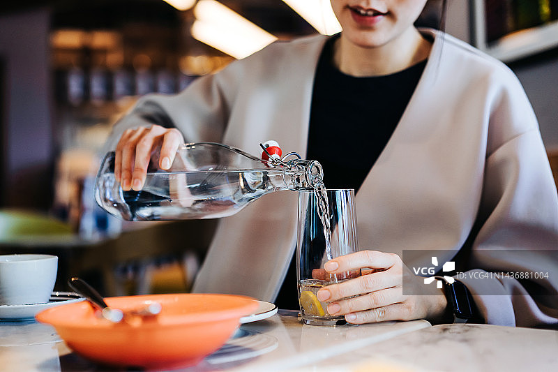 餐厅里，年轻亚洲女性倒水入杯图片素材