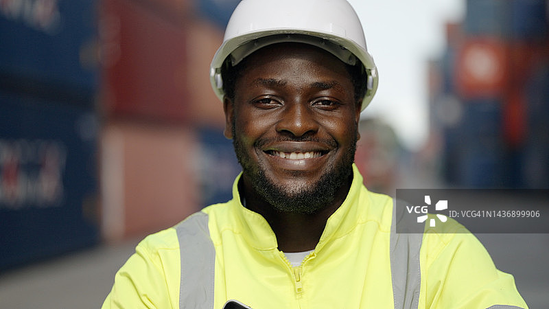 特写：戴安全帽的非裔工程师或技术员在货场工作，面带笑容图片素材