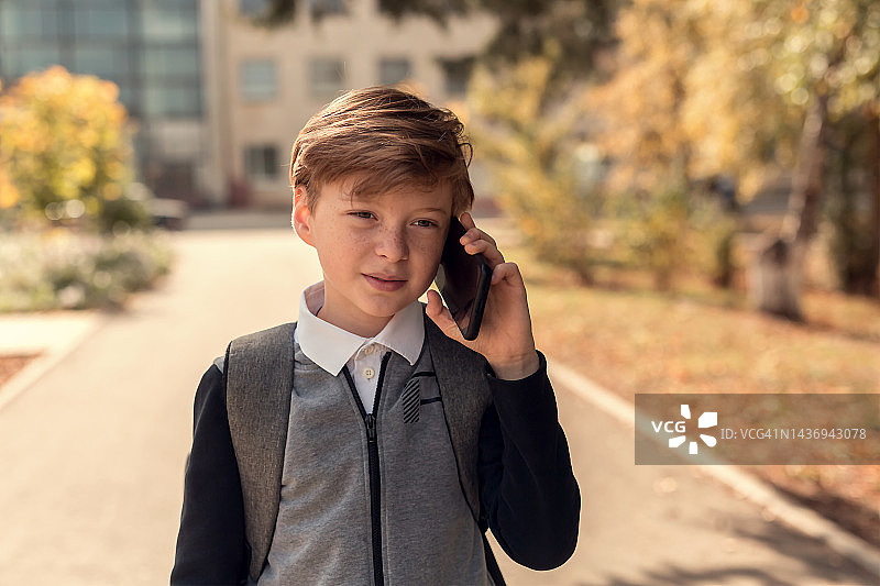 一个漂亮的金色头发男孩放学后走在街上打电话图片素材