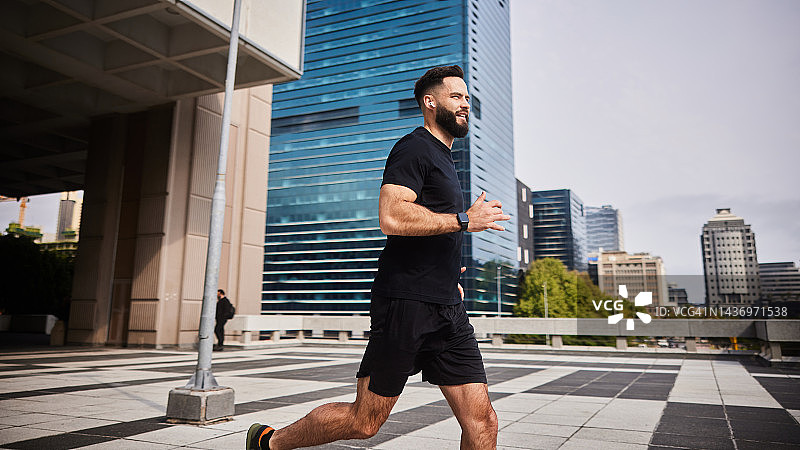 年轻男子戴着耳机在城市里跑步图片素材