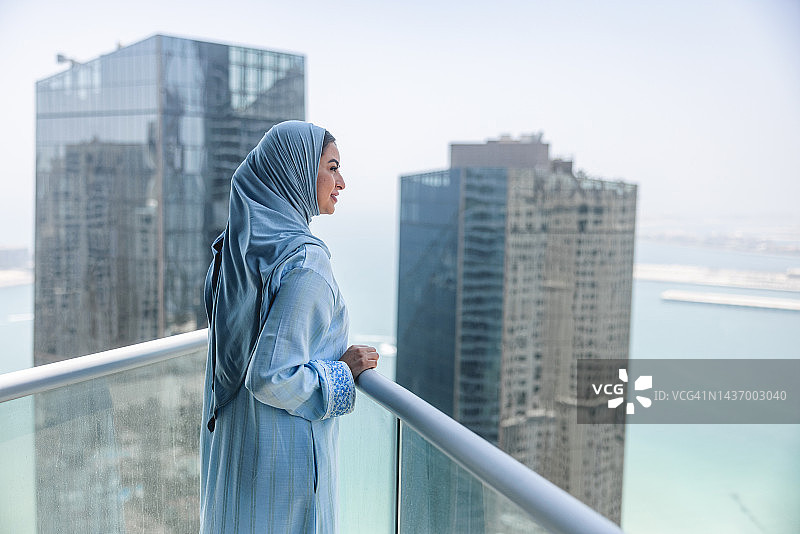 观察迪拜的中年中东女人，她在高高的阳台上，平静而快乐，焦点在前图片素材