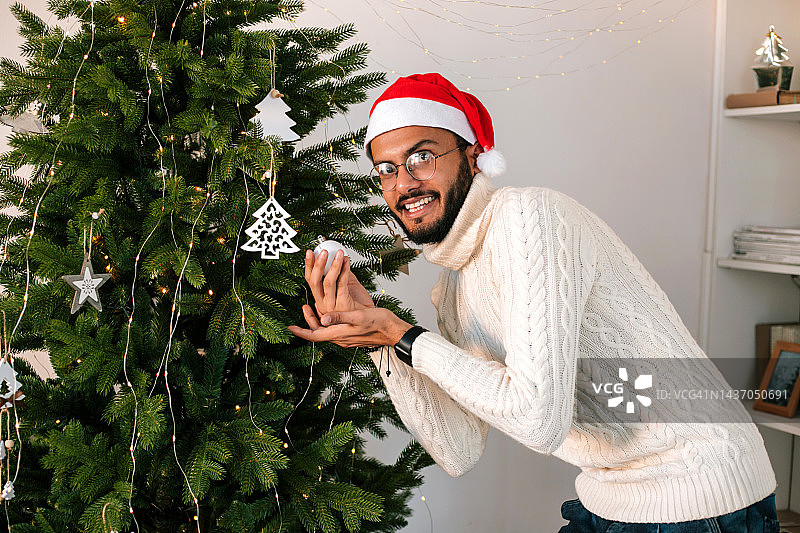 年轻的印度男子在家装饰圣诞树图片素材