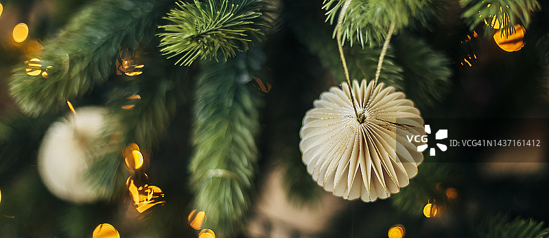 圣诞树上的米色纸球，背景为散景花环，新年概念，带有花环和装饰品的圣诞冷杉树，网站横幅图片素材
