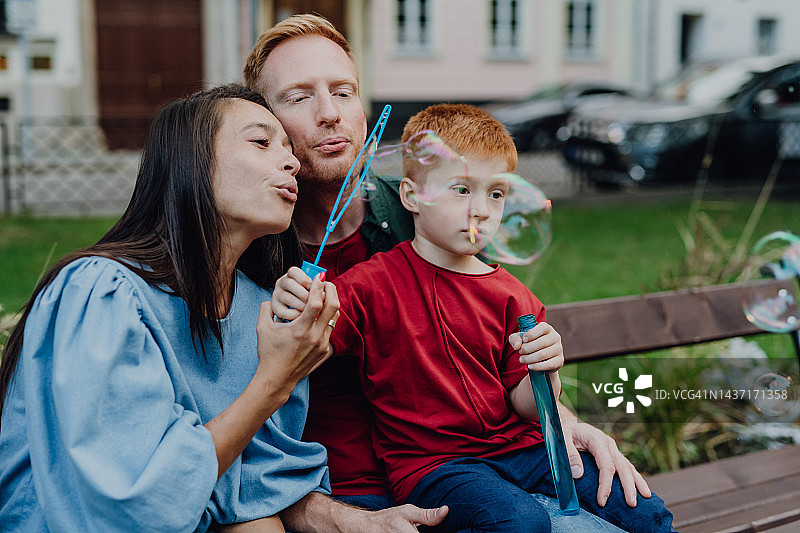 年轻家庭带着小男孩在城市里玩吹泡泡游戏图片素材