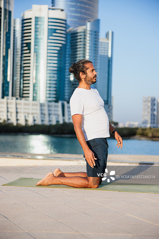 留胡子的男人在阿布扎比的码头上做瑜伽，跪在垫子上图片素材