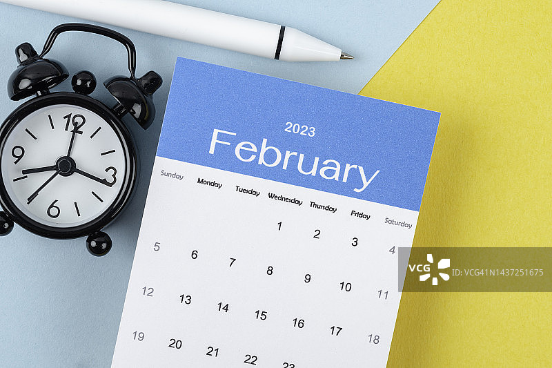 2023年台历：二月是规划和截止日期，背景为闹钟和白色笔图片素材