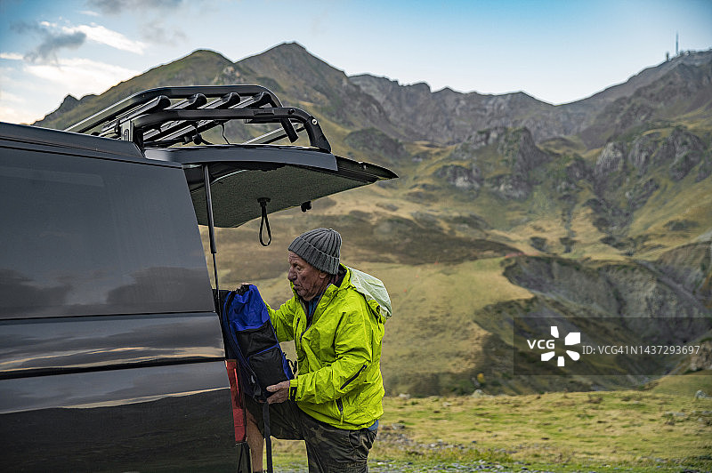 一位年长的男人在前往比利牛斯山徒步旅行前，在他的露营车后部准备背包图片素材