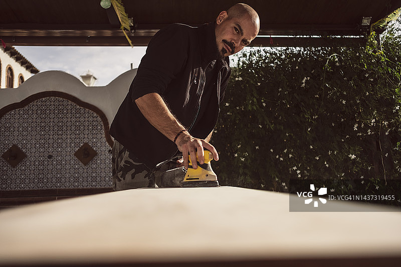 40岁男子在露台上用电动打磨机打磨桌面图片素材