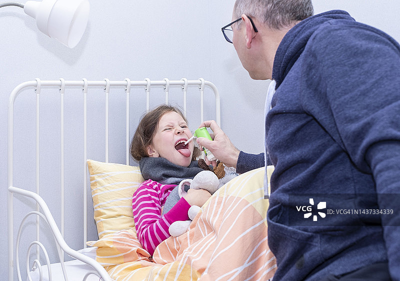 小女孩生病了，嗓子疼。男人用喷雾治疗她的喉咙。图片素材
