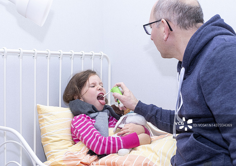 小女孩生病了，嗓子疼。男人用喷雾治疗她的喉咙。图片素材