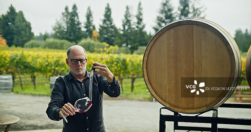 酿酒师用移液管将样品滴入桶旁的玻璃杯中图片素材