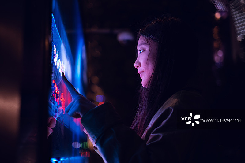 年轻的亚洲女性在夜晚的金融区使用触摸屏图片素材