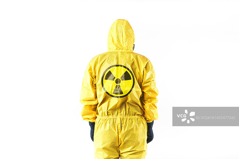 身穿黄色核防护服、戴着面罩和防护眼镜的技术员，背对白色背景上的核标志。核能与疫情概念图片素材