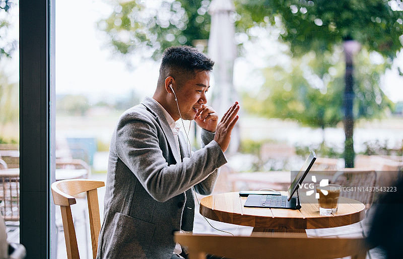 在咖啡馆使用平板电脑和耳机通过视频通话问好的快乐商人图片素材