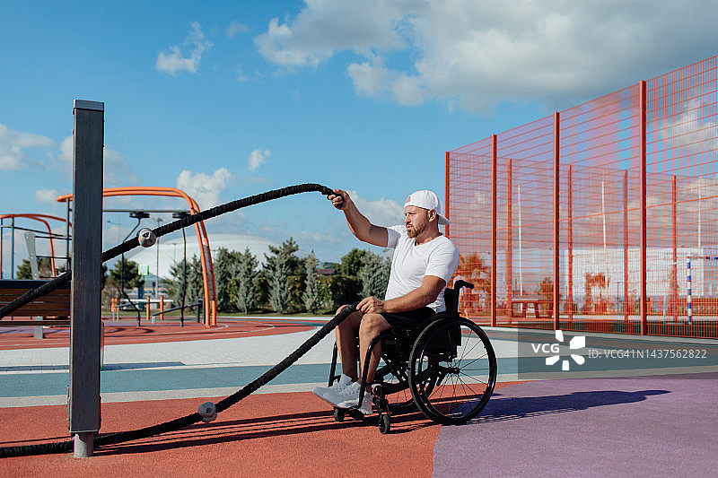 一位坐轮椅的年轻欧洲男人在运动场上进行健身运动，做绳索运动图片素材