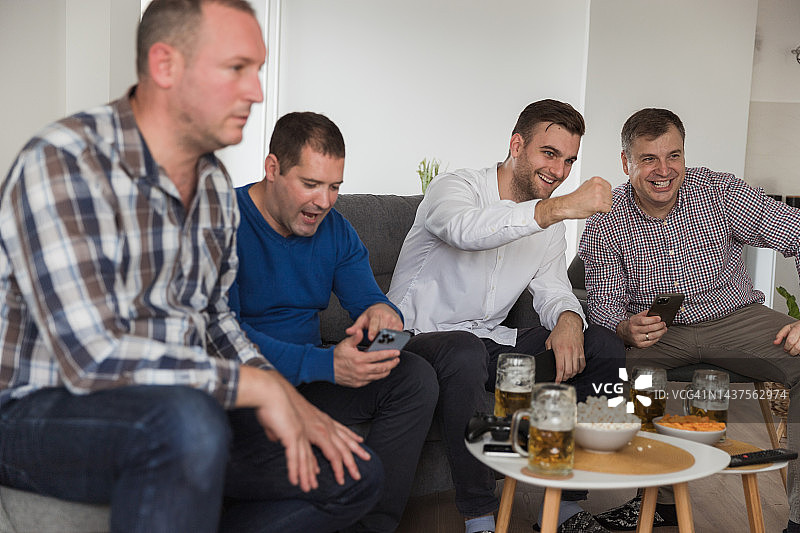 一群男人在篮球比赛电视直播期间用手机在线投注图片素材