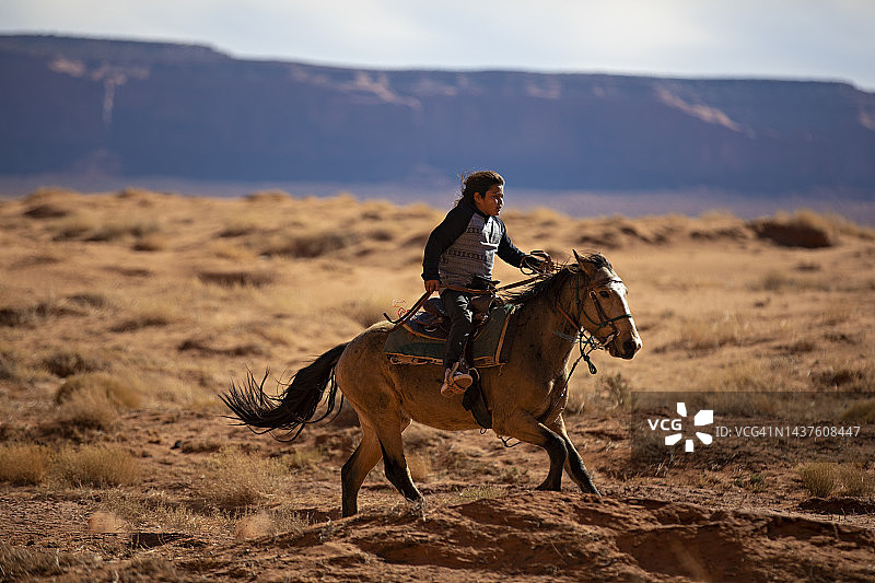 在美国亚利桑那州沙漠中骑马飞奔的纳瓦霍族男孩图片素材