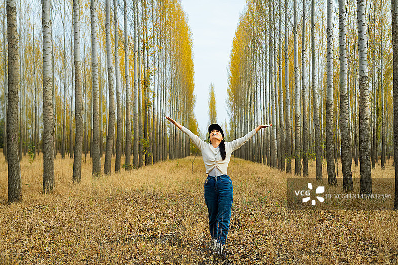 在金色的秋日森林里张开双臂的年轻女孩图片素材