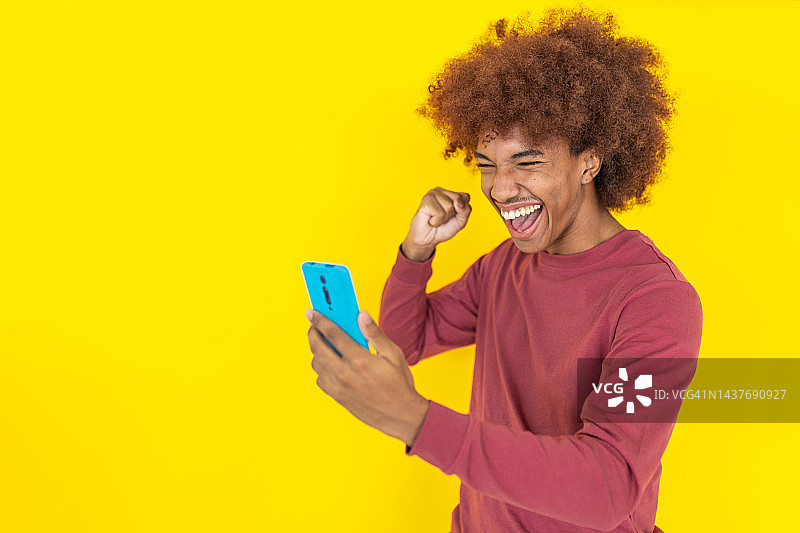 快乐的年轻非洲裔美国男人在黄色演播室背景下观看手机屏幕庆祝好消息图片素材