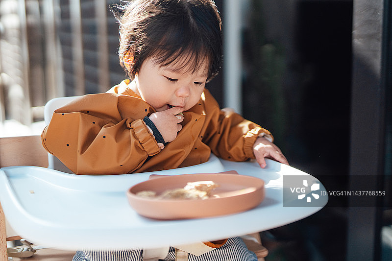 坐在高脚椅上独自吃饭的亚洲幼儿图片素材