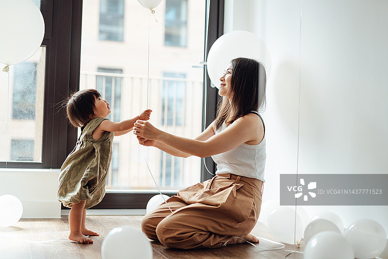 可爱的亚洲幼儿在装饰着气球的育儿室里和母亲玩耍图片素材