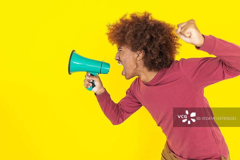 年轻非裔美国男子在黄色演播室背景下用扩音器喊叫的侧视图图片素材