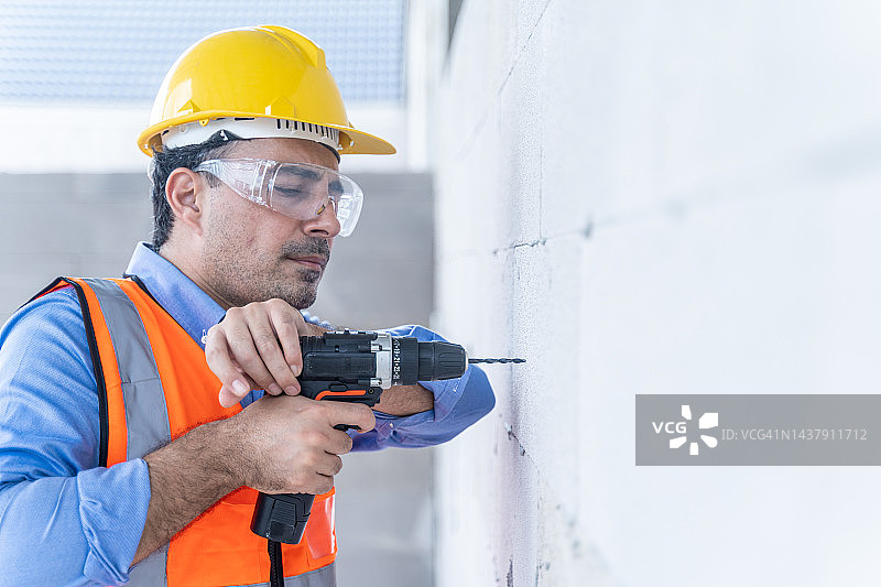 正在进行建筑工程，用钻头钻墙的男技术员图片素材