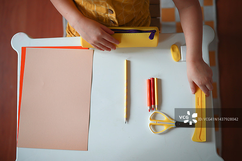 学龄前儿童在桌旁整理铅笔盒里的学习用品（俯视图）图片素材