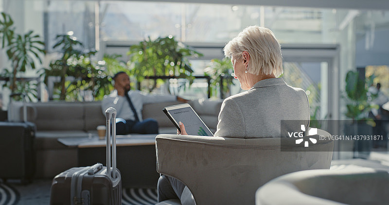 在机场候机厅使用平板电脑的商务女士，阅读股市和交易数据图片素材
