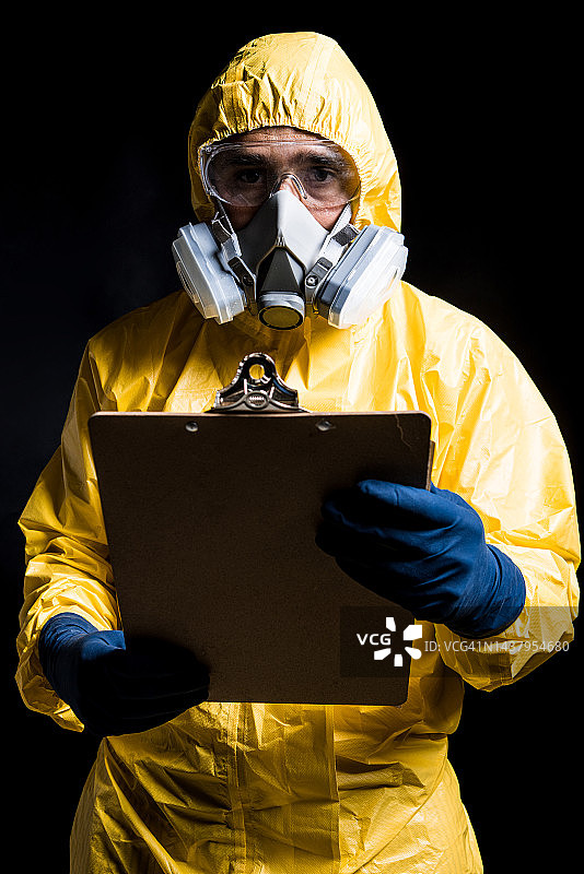身穿黄色核防护服、戴着面罩和防护眼镜的技术员手持报告文件夹的肖像图片素材