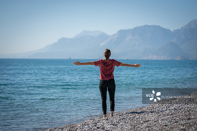 在海滩上举起双臂的快乐女子背面图片素材