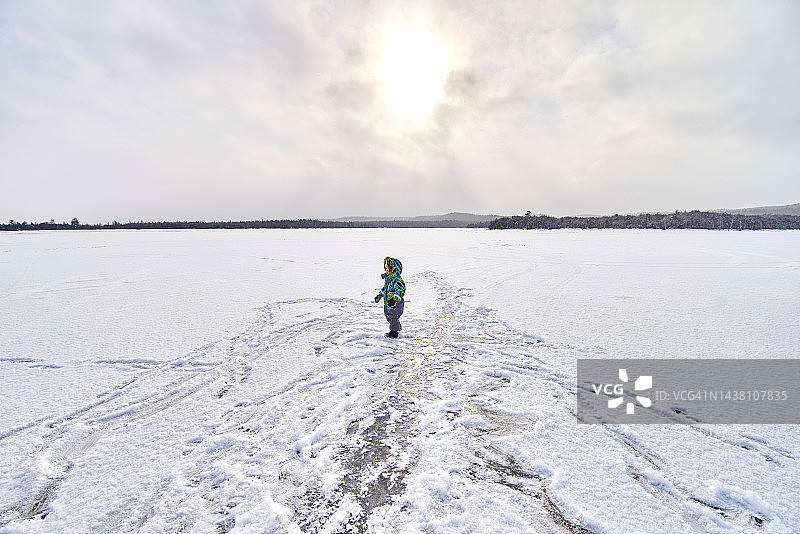 穿着冬季连体衣的女孩在冰冻的湖面上图片素材