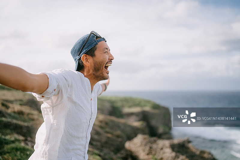 男人在海边悬崖顶上喊叫图片素材
