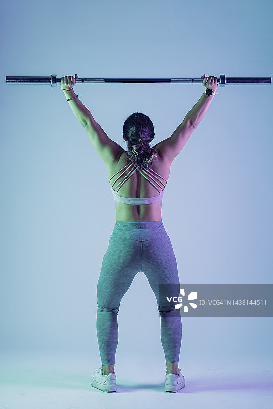 穿着运动服的女人从背面做杠铃举重图片素材