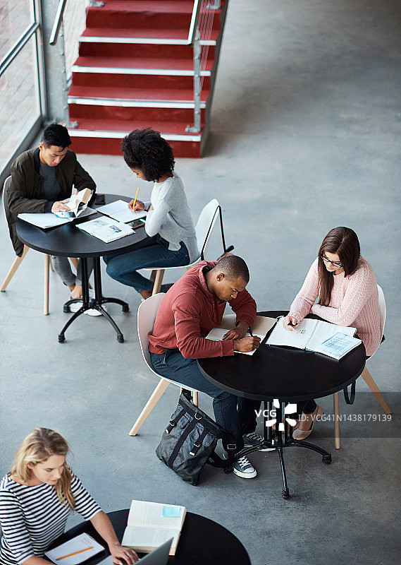 在校园自习室或图书馆的工作区学习、讨论和规划项目的学生。年轻人从上方一起写笔记，获取大学知识图片素材