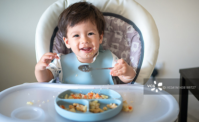 15个月大的男婴在家用勺子自己吃饭图片素材