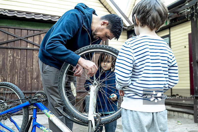 男子在屋外和儿子们一起修理自行车轮图片素材