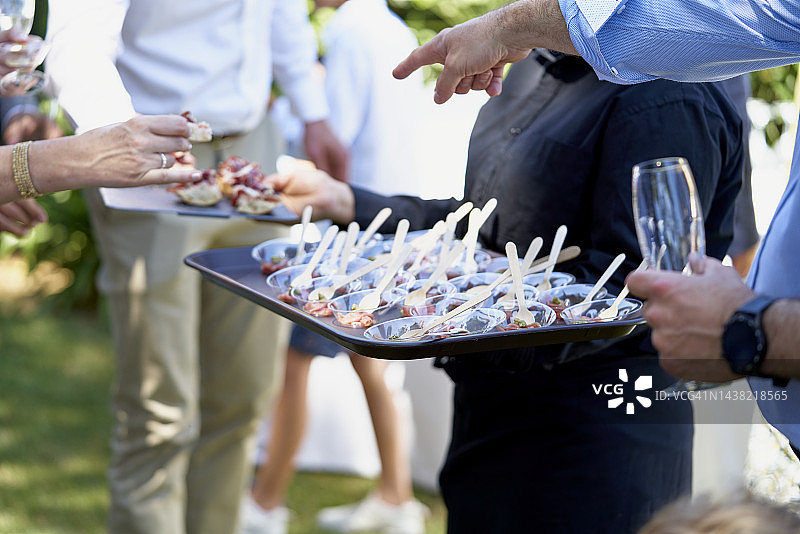 服务员在优雅的社交活动中为穿着考究的客人提供开胃菜的局部照片图片素材